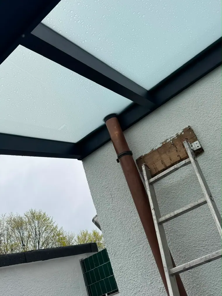 Blick von unten auf die Dachfüllung einer frisch montierten Terrassenüberdachung, Regenwasser läuft über die Platten ab