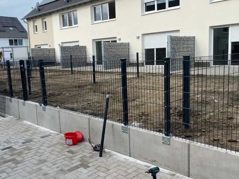 Neu gesetzter Doppelstabmattenzaun mit Gabionen-Pfosten an einem Neubau